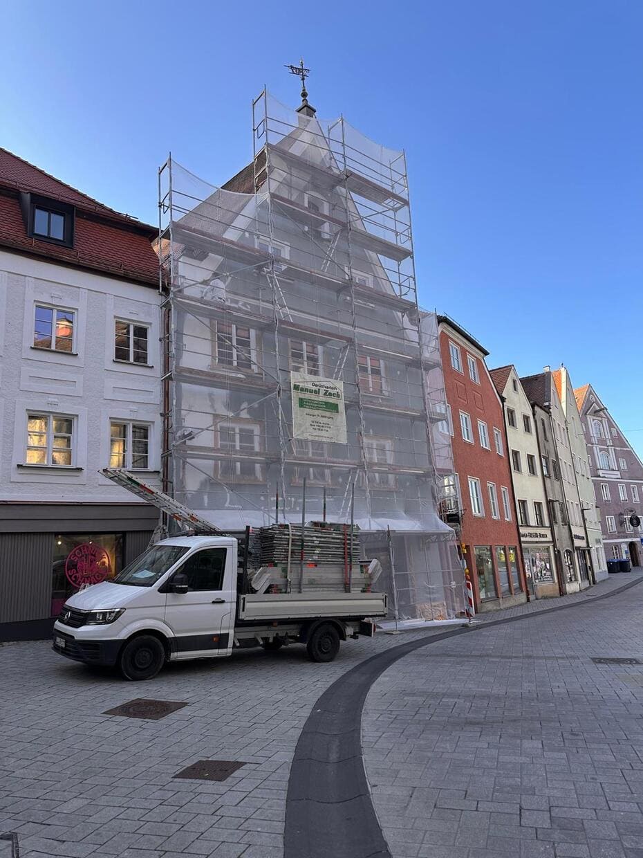 Abb. Gerüstbau in Landsberg am Lech - vordere Häuserfasade ist eingerüstet inkl. Sicherheitsnetz. Davor steht ein weißer Transporter mit Ladefläche und weiterem Gerüstmaterial.